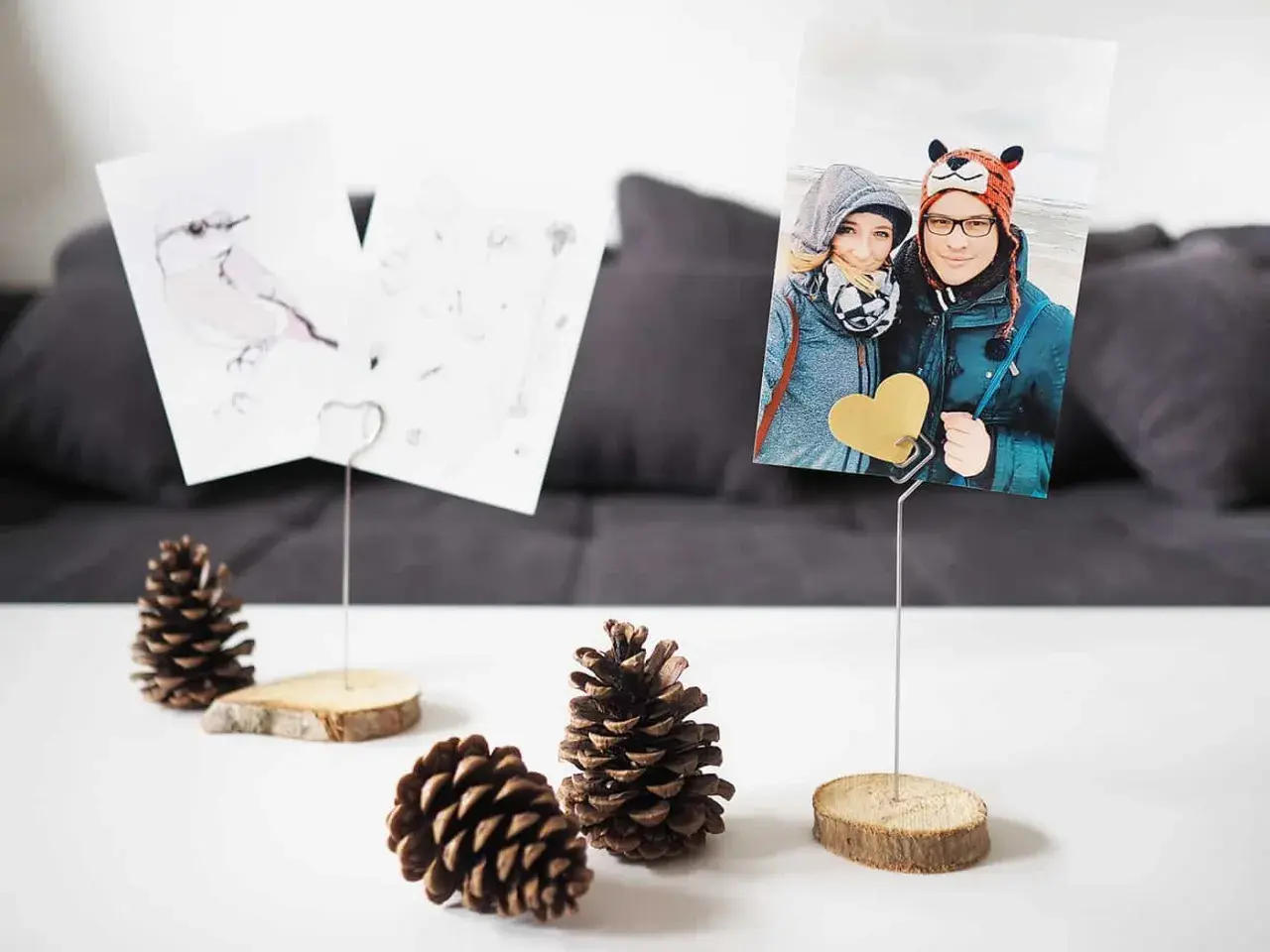 Selbstgemachte Fotohalter aus Holzscheiben und Draht mit Fotos von einem Paar und einem Vogel. Perfekt, um Erinnerungen zu präsentieren.
