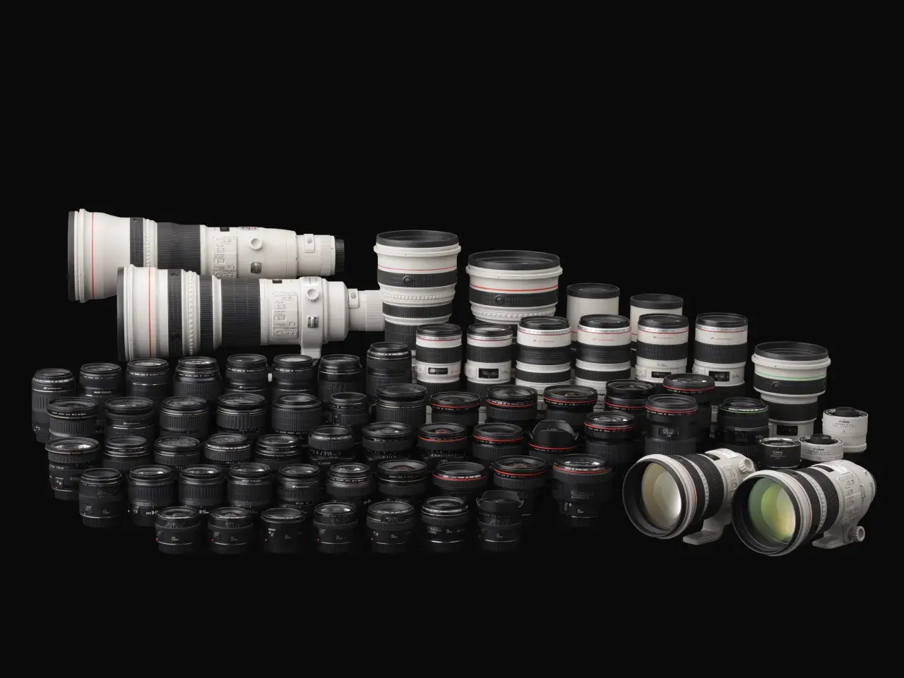 Vasta collezione di obiettivi per fotocamere, con diversi modelli e marche di macchine fotografiche, disposti su sfondo nero.