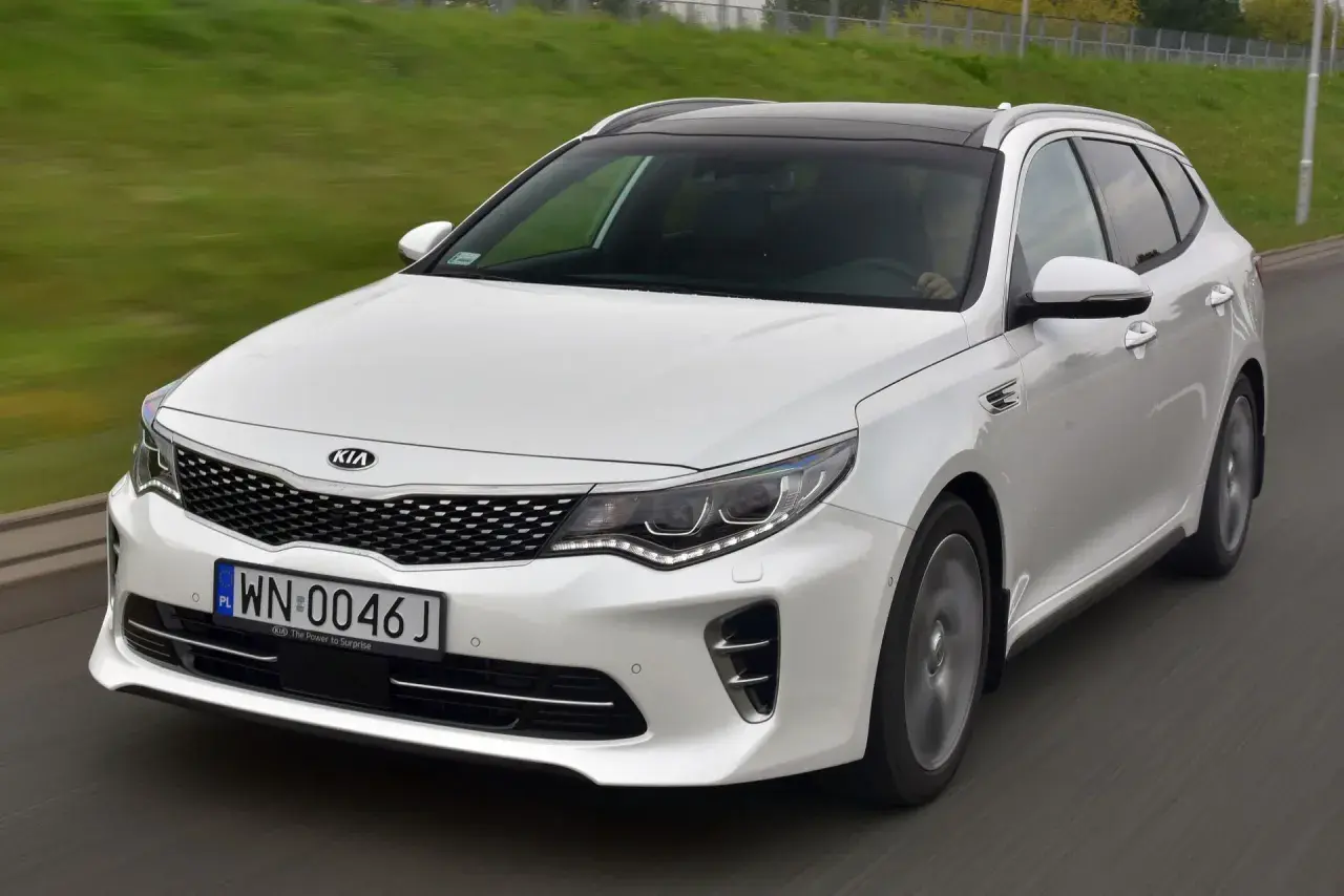 Biała Kia Optima w wersji kombi na drodze. Wiele osób szuka kia optima opinie przed zakupem.