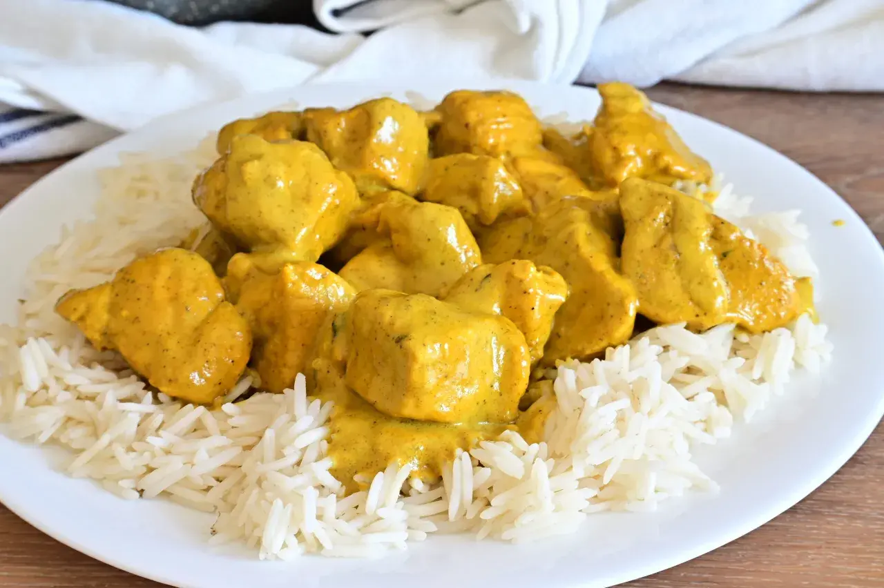 Piatto di riso basmati con saporito pollo al curry, ricoperto da una cremosa salsa gialla.