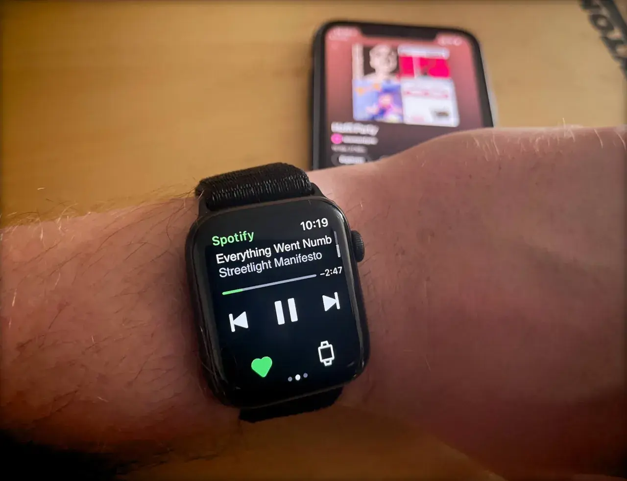 Apple Watch zeigt Spotify-Song "Everything Went Numb" von Streetlight Manifesto. Ein iPhone im Hintergrund spielt ebenfalls Musik.