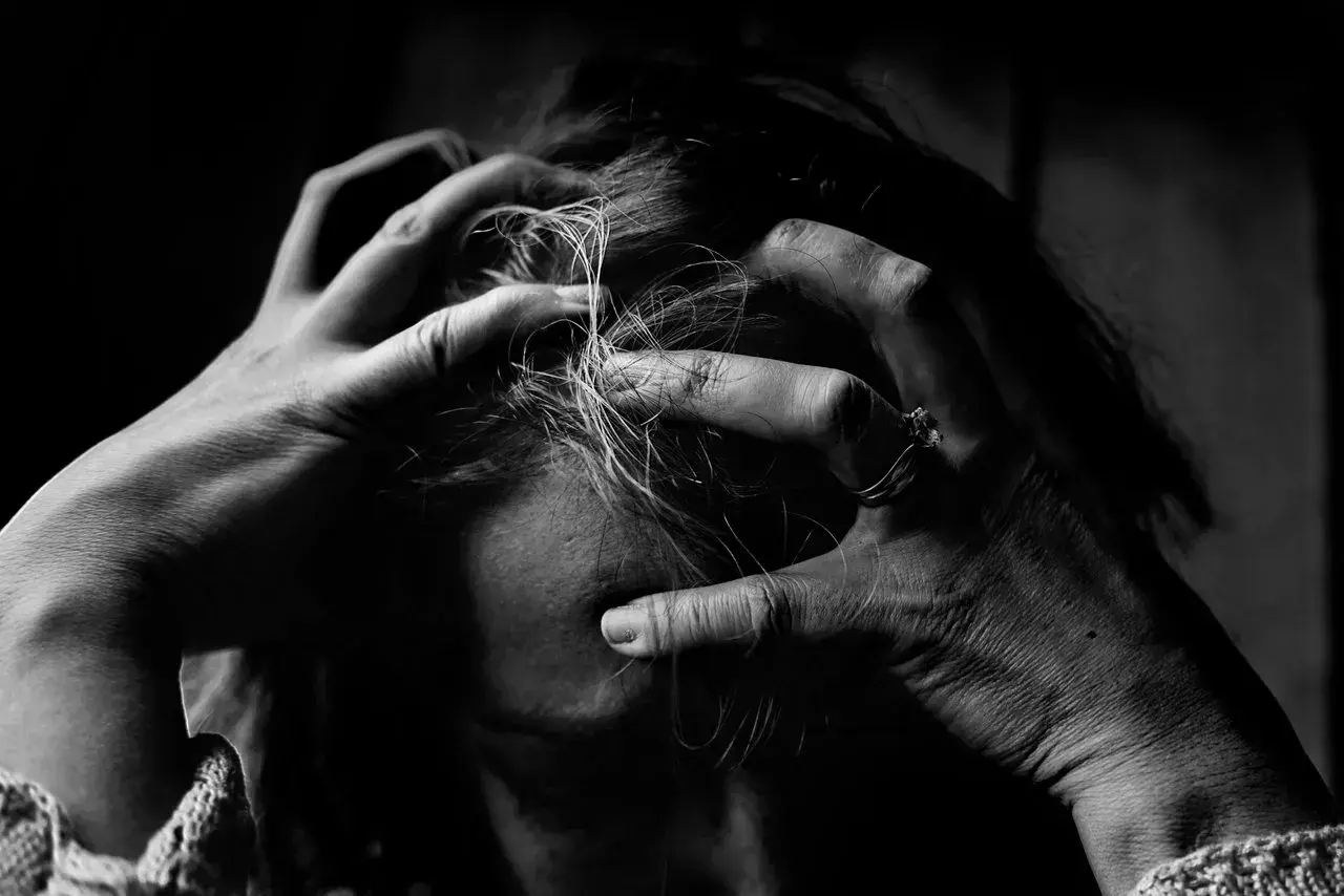 Dłonie zaciskają się na włosach, symbolizując wewnętrzną walkę i dewaluację psychologiczną.