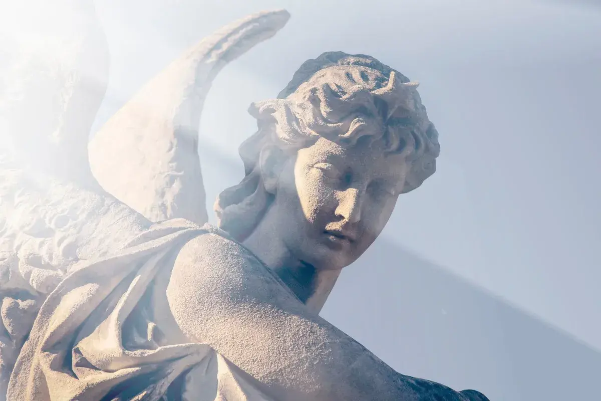 Kamienna rzeźba anioła, z promieniem światła padającym na twarz. W ciszy serca rodzi się modlitwa do anioła stróża o pomoc.