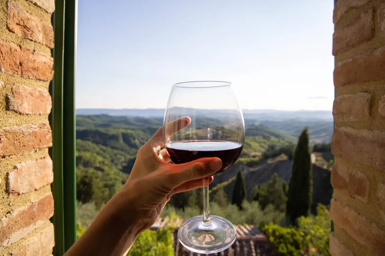 Un bicchiere di vino rosso, con il paesaggio del Val d'Orcia sullo sfondo. Un momento di puro piacere.