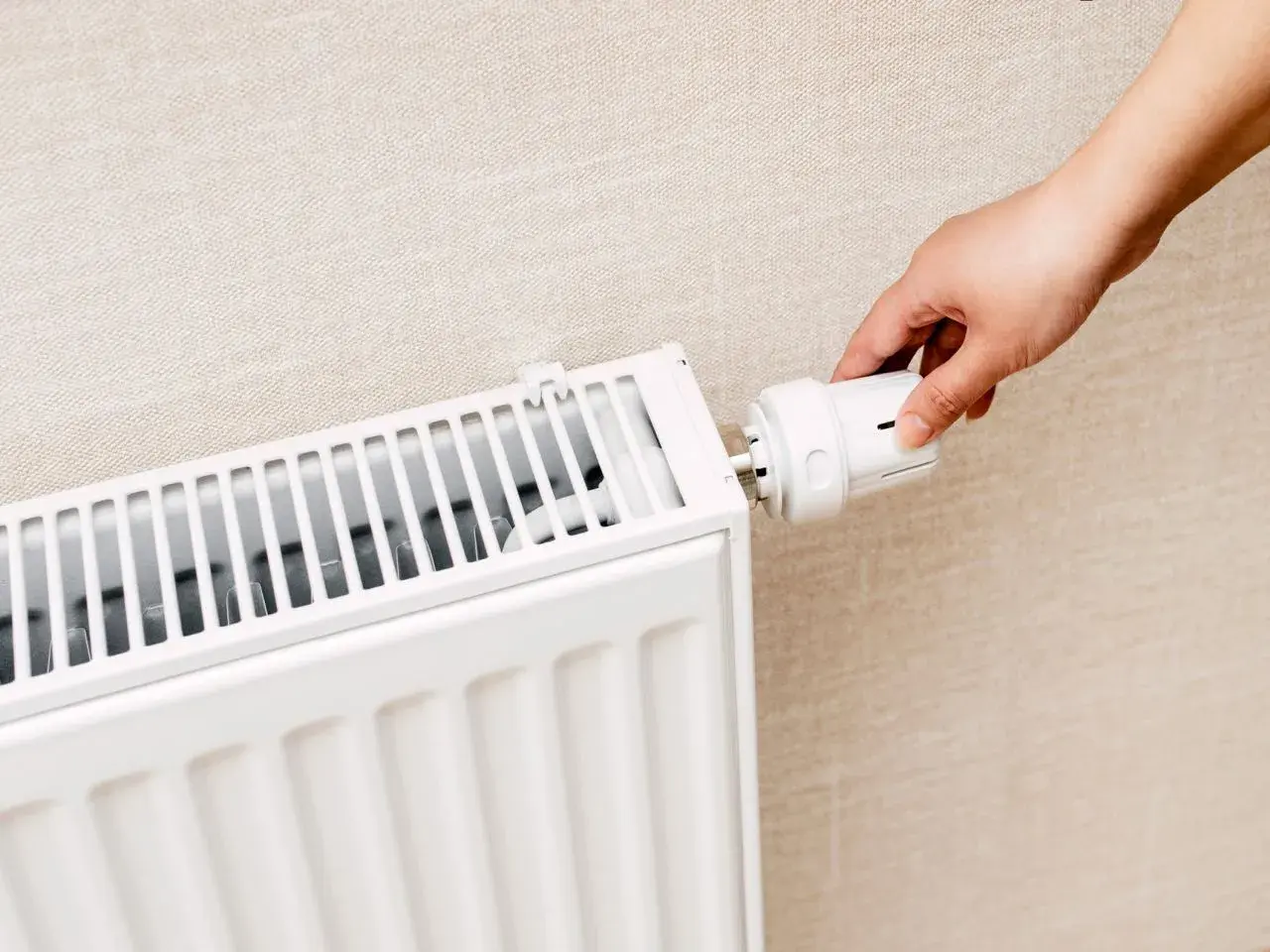Dłoń reguluje termostat grzejnika. Czy zakręcać grzejniki na noc? To pytanie o oszczędność energii.