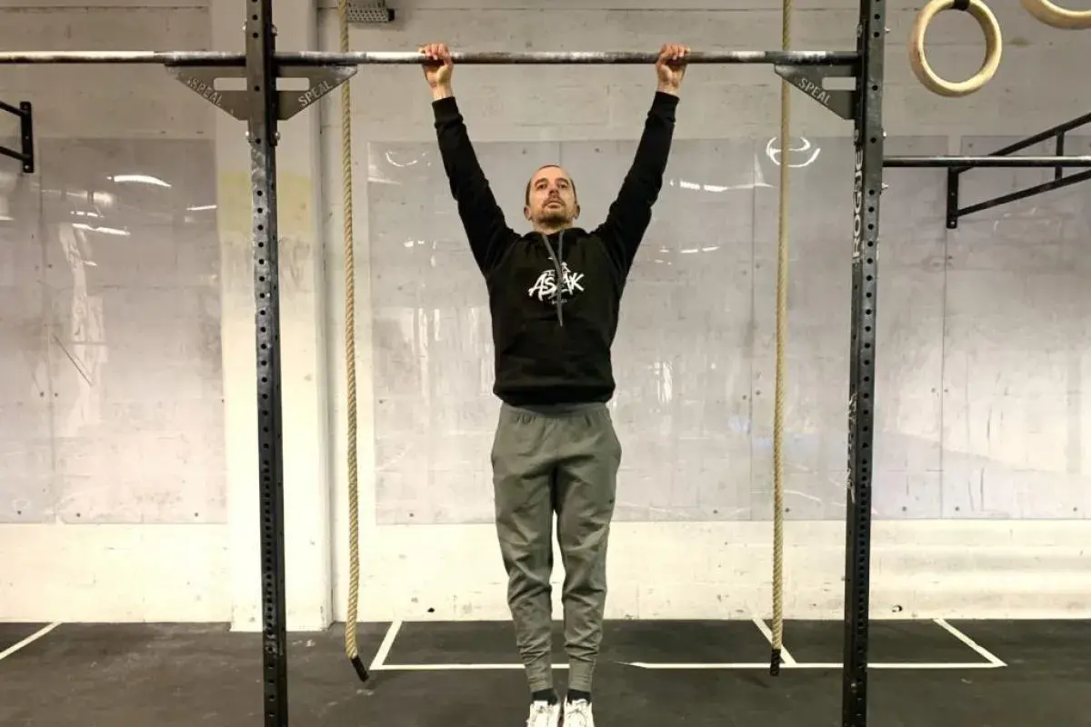 Un homme en tenue de sport s'accroche à une barre de traction, prêt à commencer son programme traction.