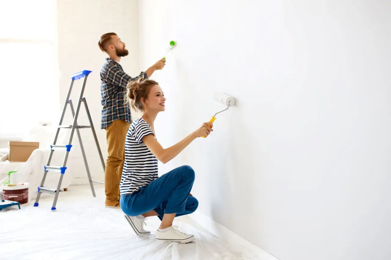 Coppia felice imbianca casa con rullo, trasformando le pareti bianche in un nuovo inizio.