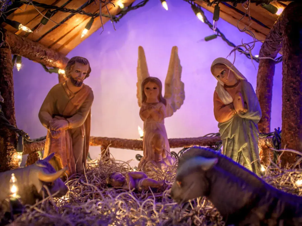 Portal de Belén manualidades: figuras de San José, la Virgen María, un ángel, el Niño Jesús, un buey y una mula, iluminados con luces navideñas.
