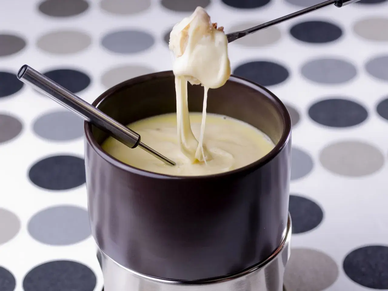 Un morceau de pain trempé dans une fondue au comté crémeuse, filant sur une fourchette.