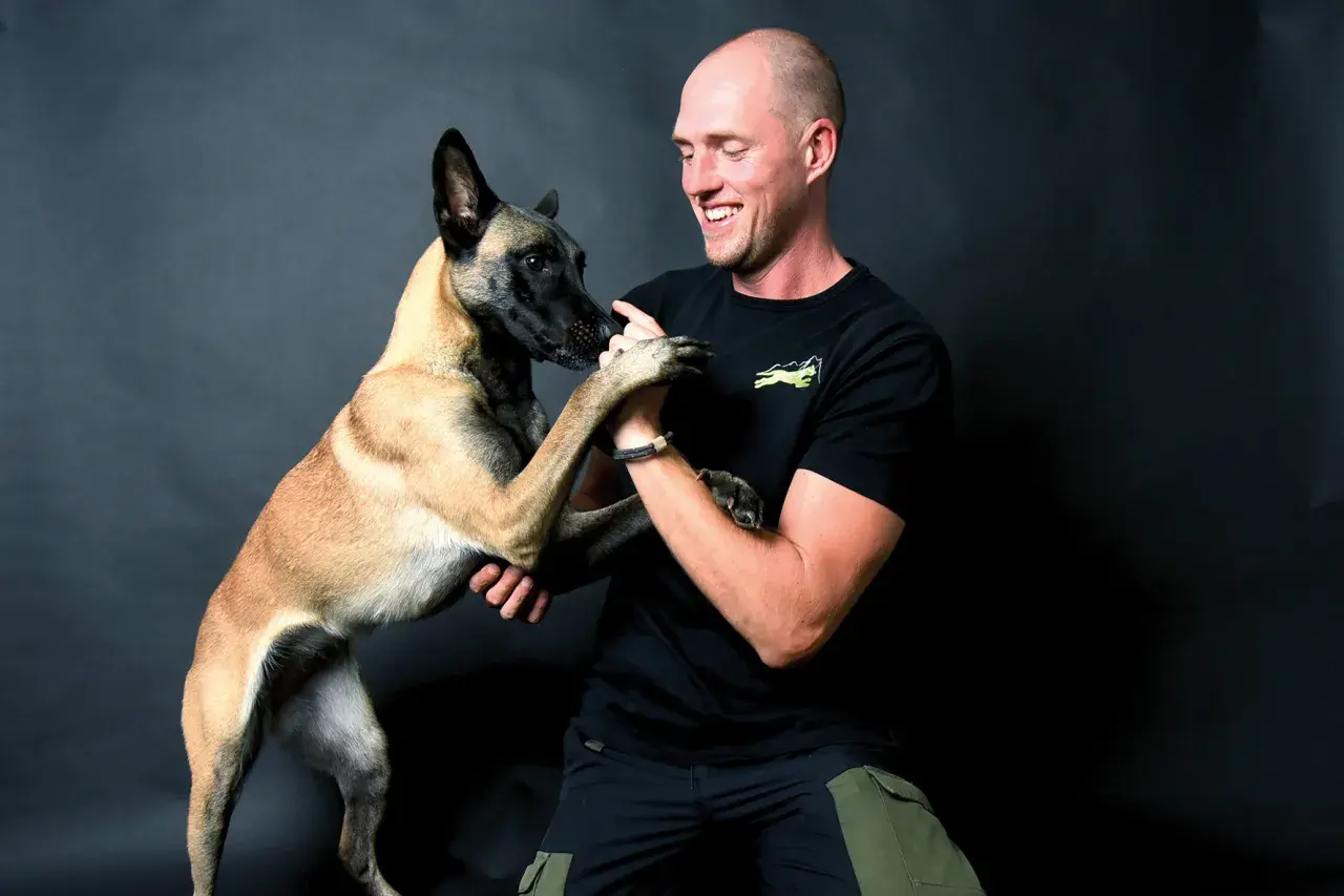 Ein Mann lacht und hält die Pfoten seines Malinois. Erfolgreiches Hunde Training zeigt die enge Bindung.