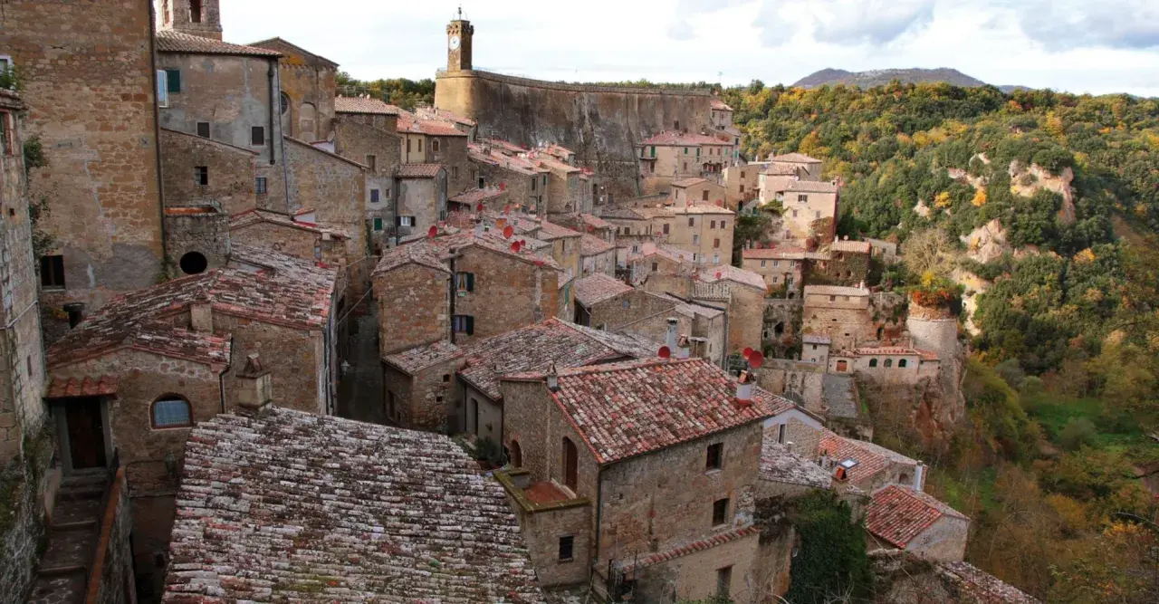 Sorano, Toscana: un borgo medievale arroccato su una rupe tufacea, con tetti rossi e case in pietra che si fondono con il paesaggio autunnale.