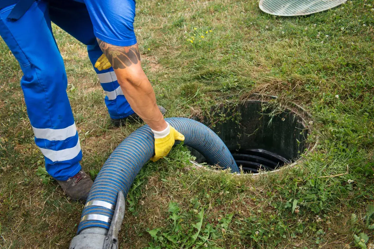 Pracownik w żółtych rękawiczkach wkłada gruby wąż do szamba, pokazując, jak zrobić odpływ.