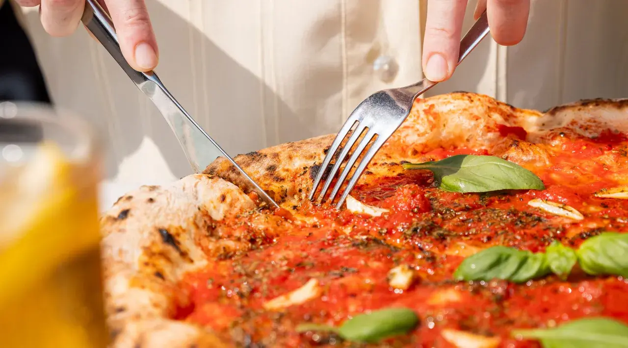 Eine Pizza Marinara wird mit Messer und Gabel angeschnitten.