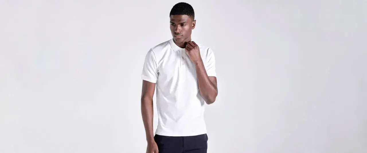 Ein Mann in einem weißen Poloshirt, das klassische Merkmale wie den Kragen und die Knopfleiste zeigt.
