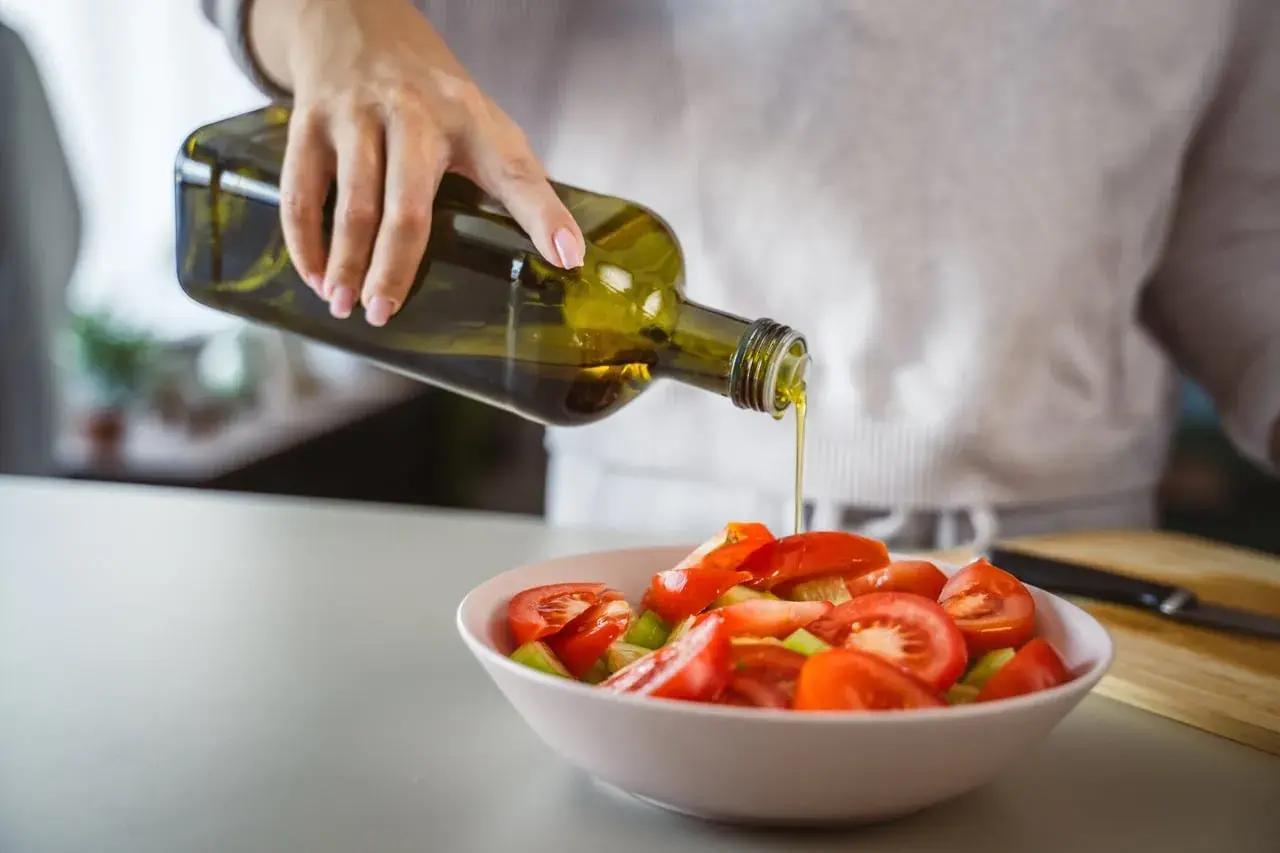 Une main verse de l'huile d'olive cuite sur une salade de tomates. Une touche saine pour contrôler le cholestérol.