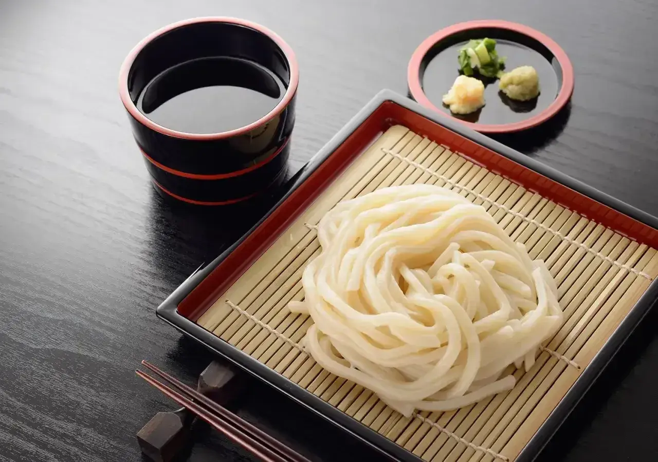 Prosty makaron udon przepis: grube kluski na bambusowej macie, miseczka z sosem i dodatkami. Idealne danie.