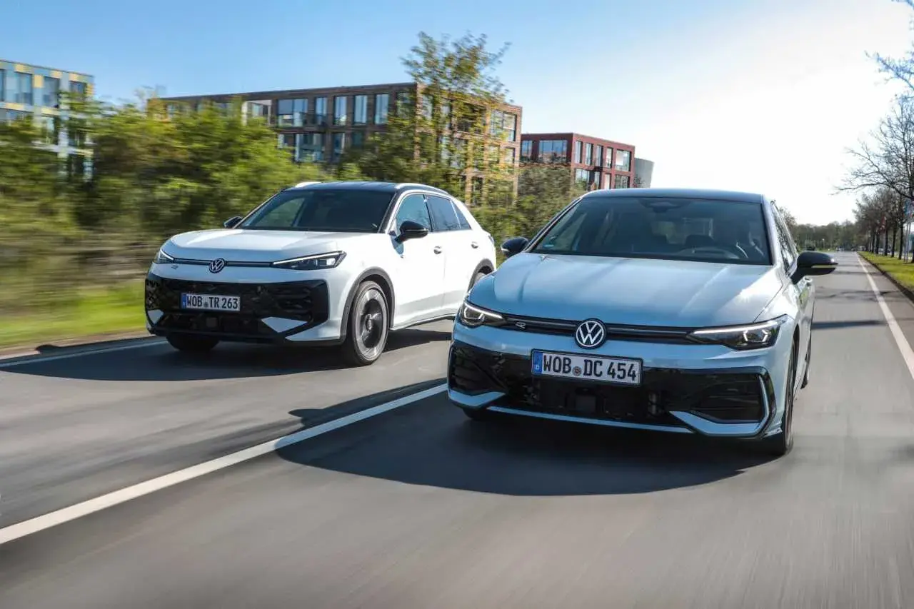 Två Volkswagen-bilar, en vit SUV och en ljusblå sedan, kör på en väg. Den vita bilen ser ut som en t-roc hybrid.