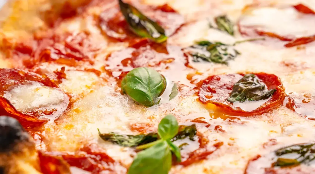 Nahaufnahme einer Pizza mit geschmolzenem Käse, roten Salami-Scheiben und frischem Basilikum. Verschiedene Salami-Sorten machen diese Pizza unwiderstehlich.