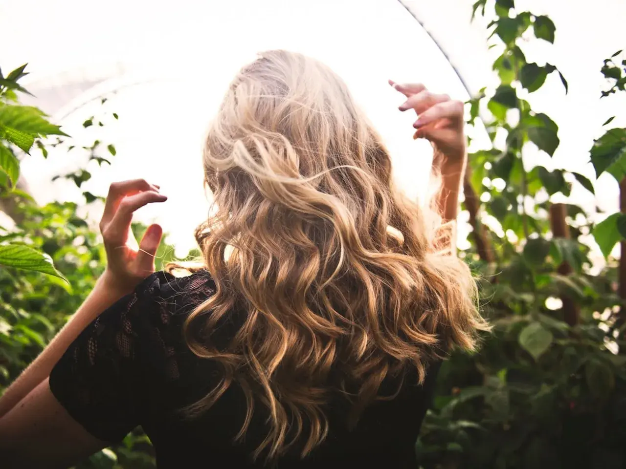 Blondes Haar mit Beach Waves im Sonnenlicht, umgeben von grünen Blättern.