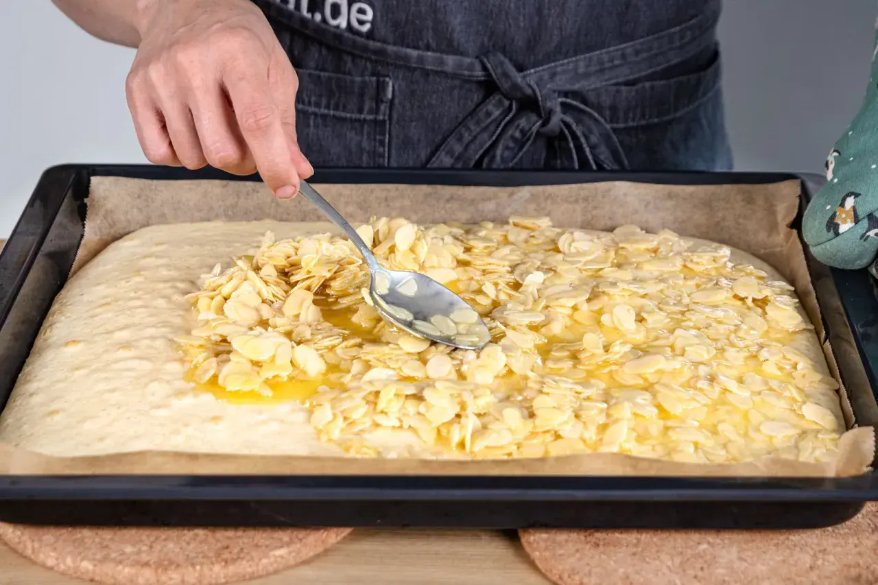 Mit einem Löffel werden Mandelblättchen auf den Teig für ein Blitzkuchen Rezept verteilt.