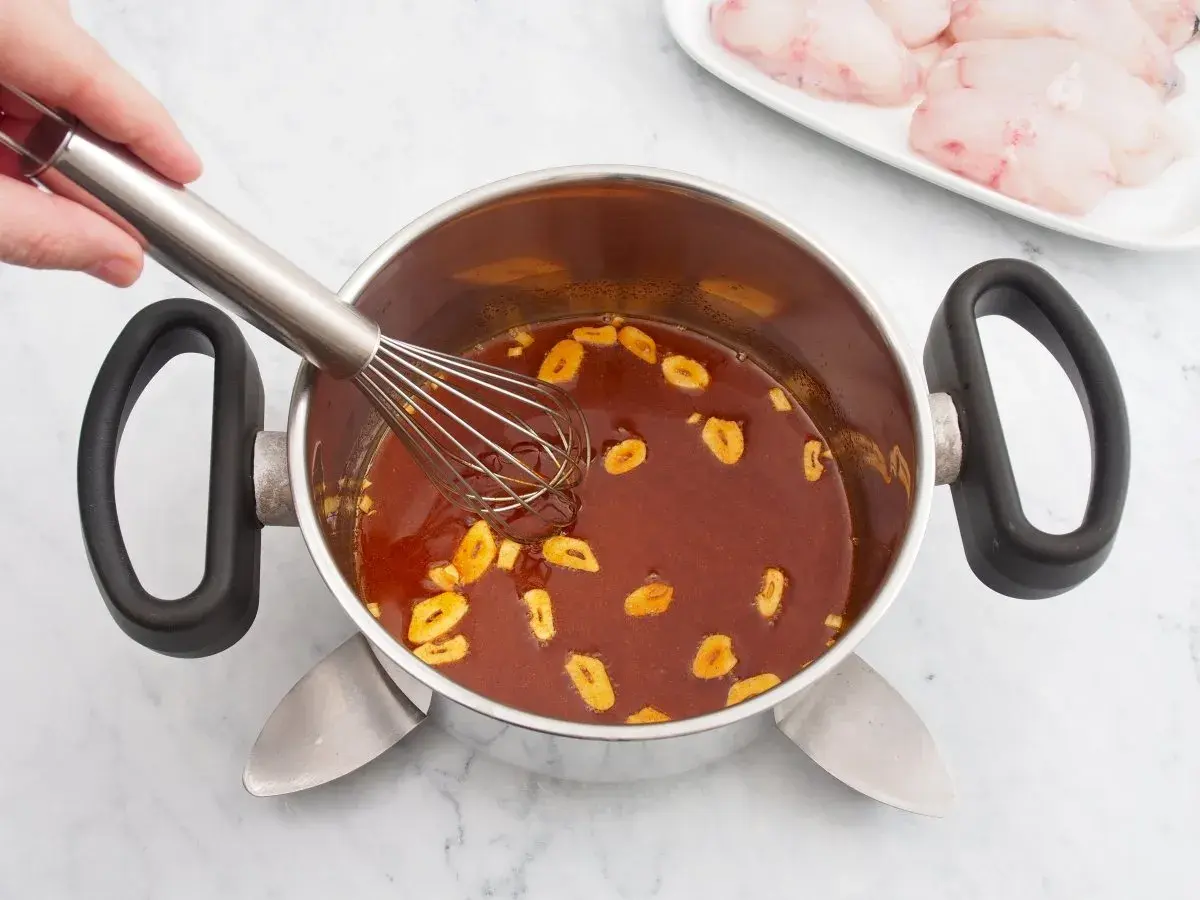 Batir salsa con ajo en una olla. En un plato, trozos de rape fisch listos para cocinar.