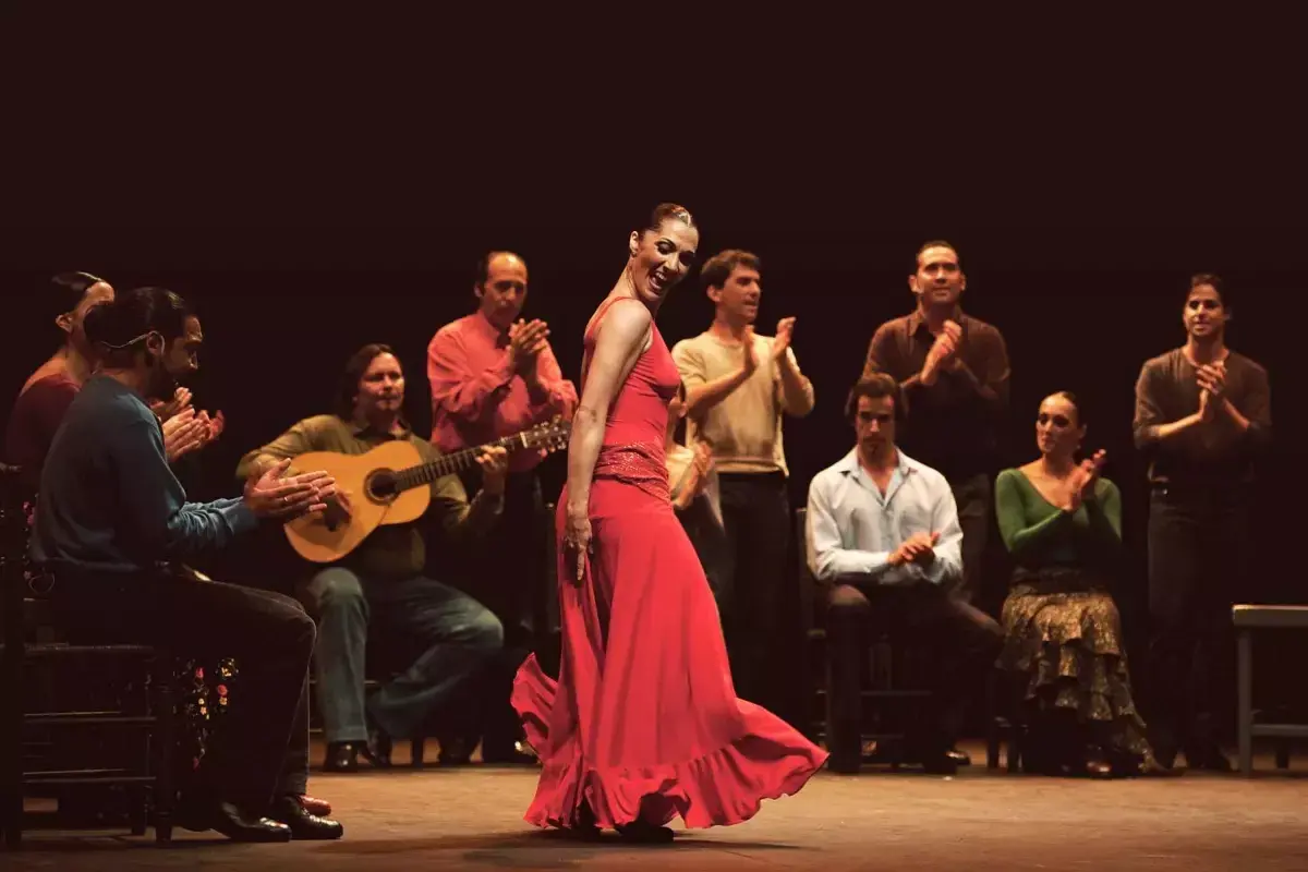 Una vibrante artista flamenco, con un vestido rojo, baila apasionadamente mientras músicos la acompañan.