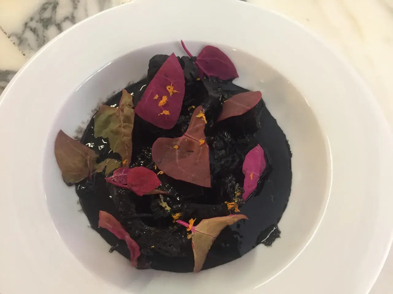 Un plat de ragout de seiche à l'encre noire, garni de pétales de fleurs séchées et d'une touche d'agrume.