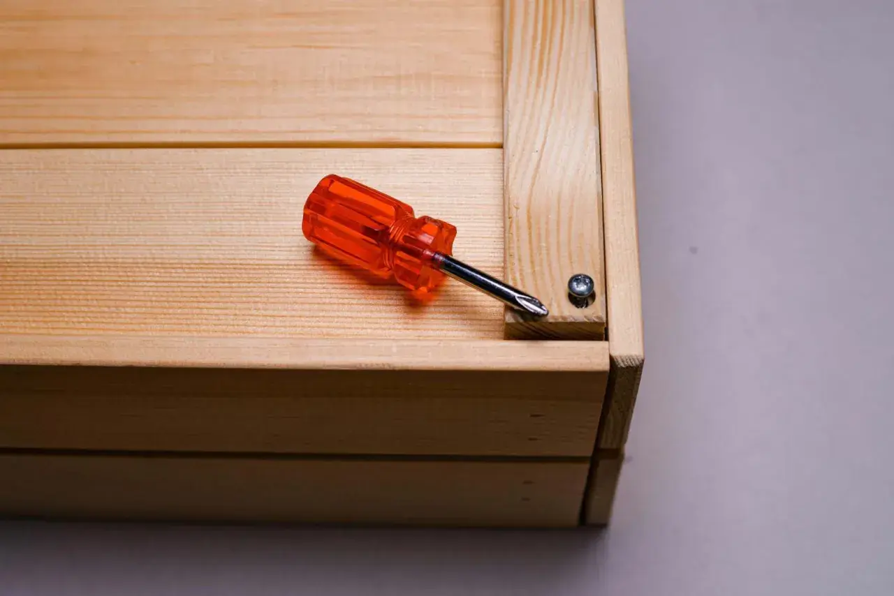 Cacciavite arancione su un mobile in legno grezzo, pronto per essere restaurato.