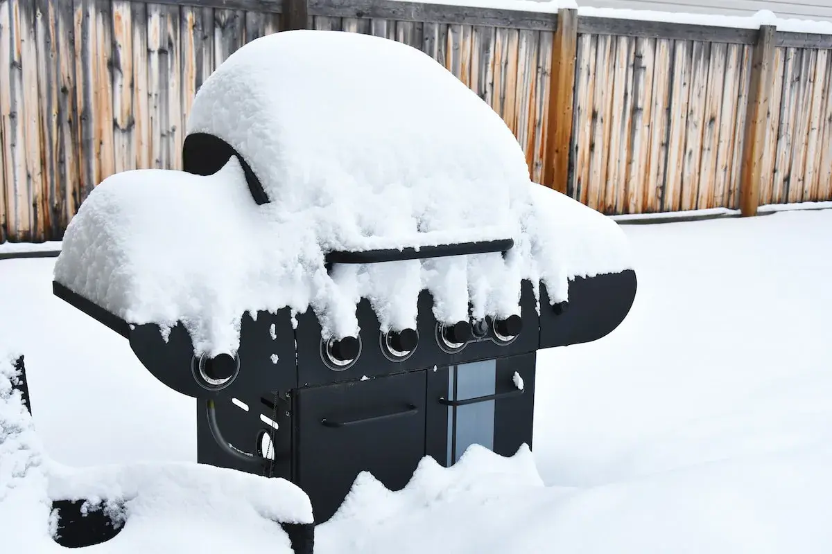 En snötäckt gasolgrill under tak, redo för sommarens grillkvällar trots vinterns kyla.