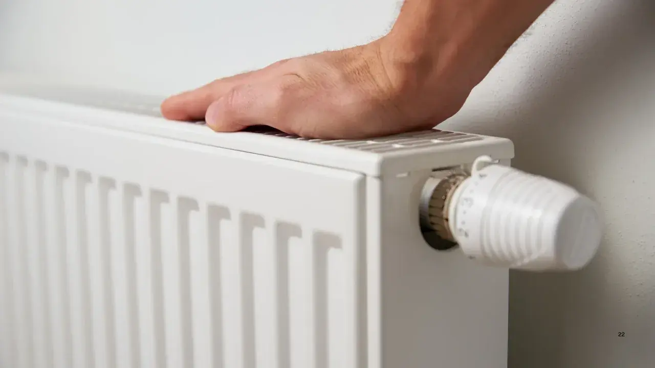 Mano sobre radiador blanco, ajustando el termostato. Es hora de decidir cuándo poner la calefacción para estar cómodo.