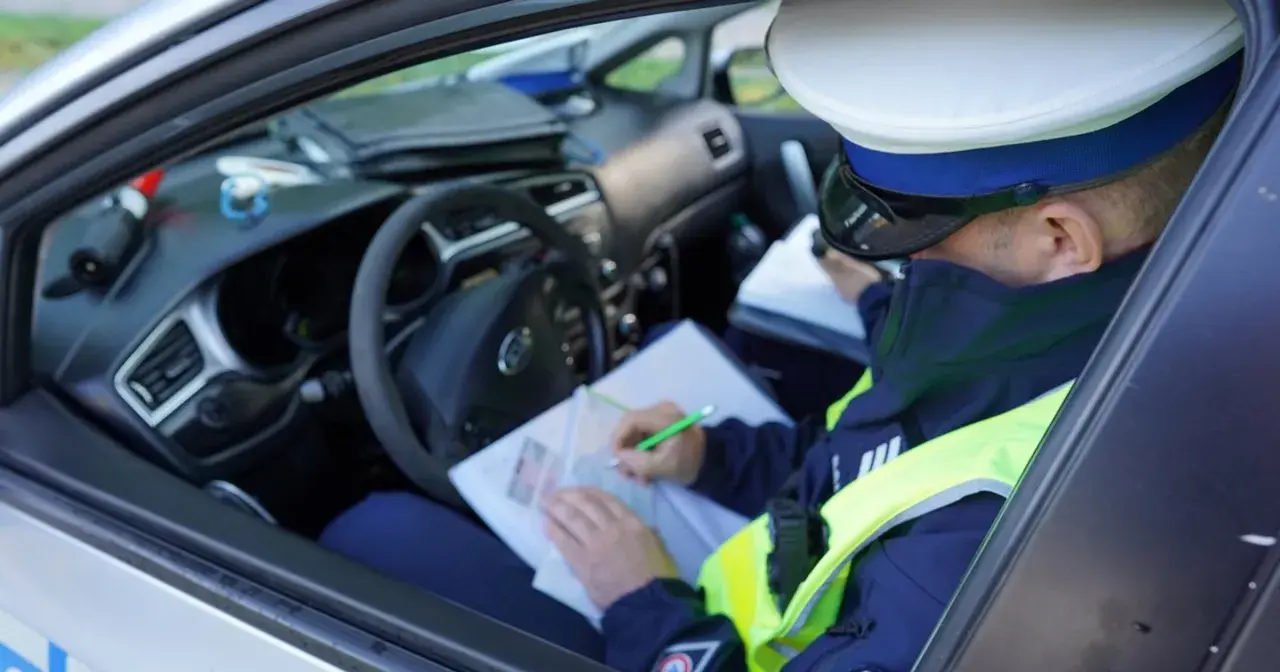 Policjant w radiowozie spisuje mandat za jazdę bez kasku.