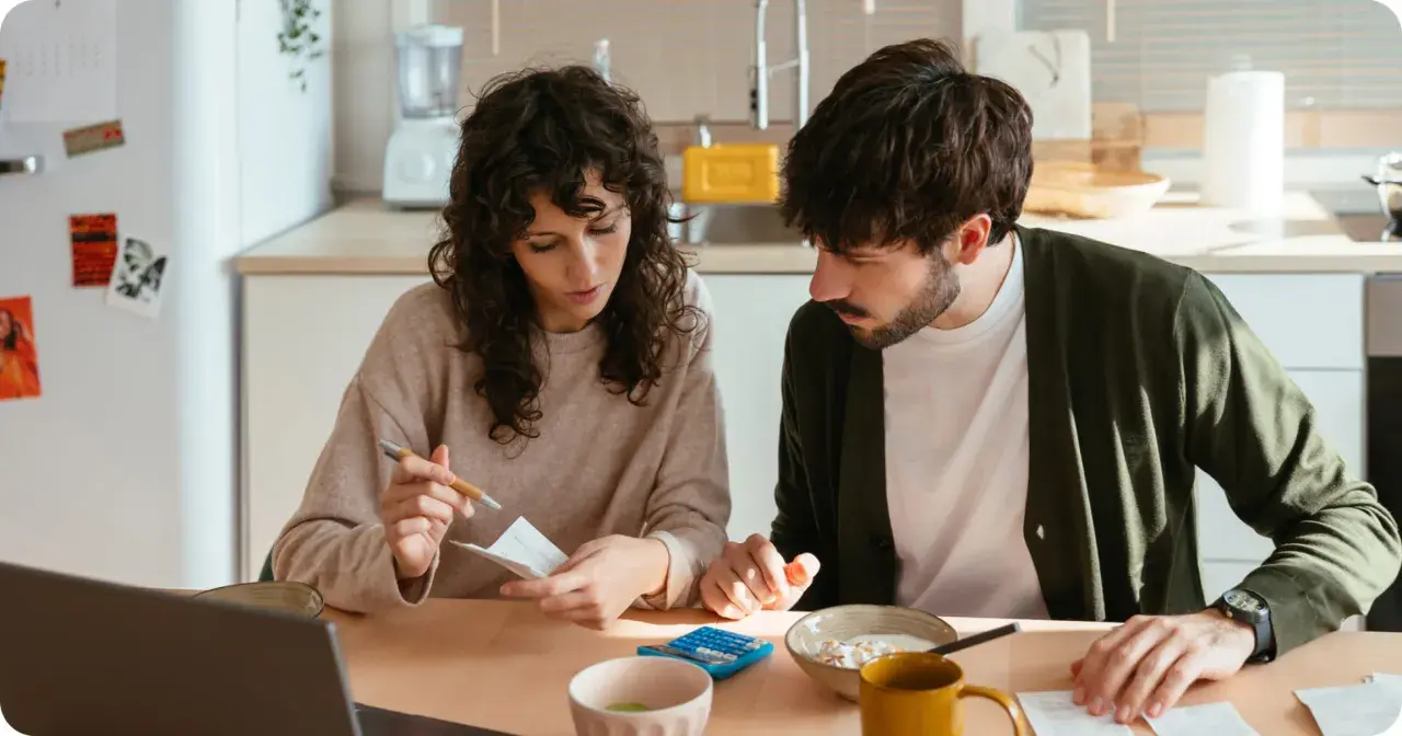 Pareja revisando facturas y usando calculadora, gestionando su comunidad de bienes entre familiares.