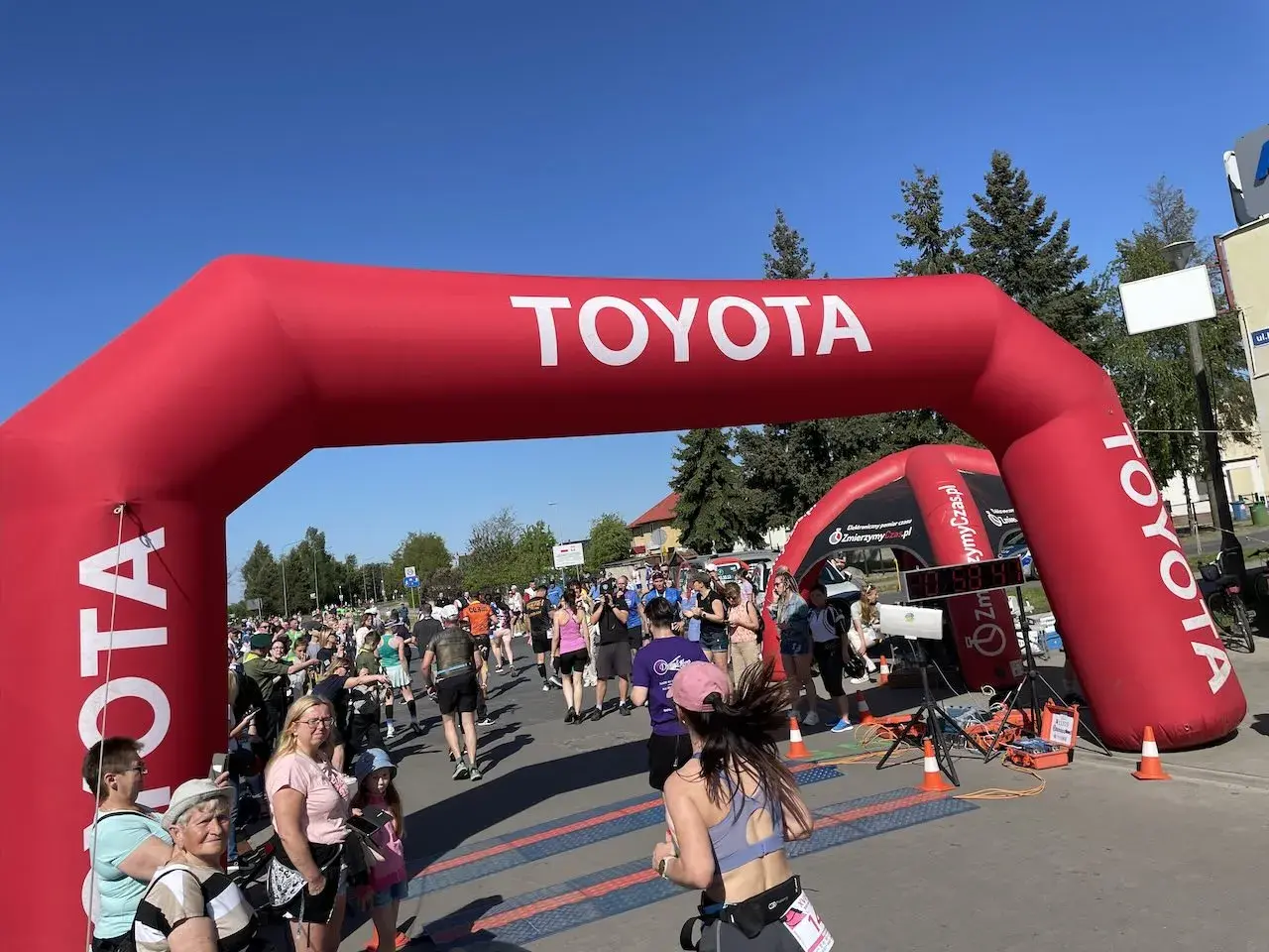 Uczestnicy biegną pod czerwonym łukiem Toyoty. Czy to już koniec półmaratonu? Jaki dystans pokonali?