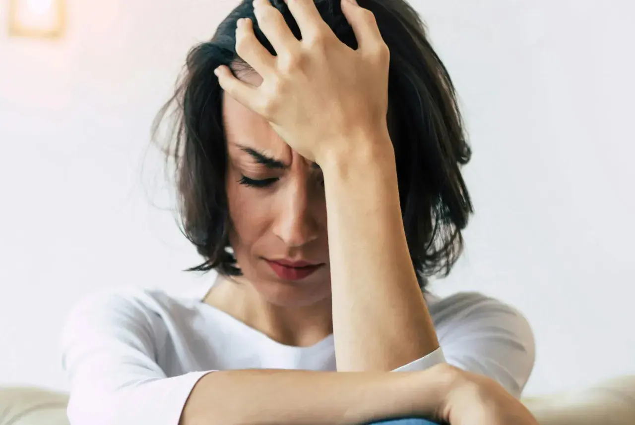 En kvinna med handen mot pannan, ansiktet nedåt, visar tydliga tecken på depression och dess fysiska symptom som huvudvärk och utmattning.