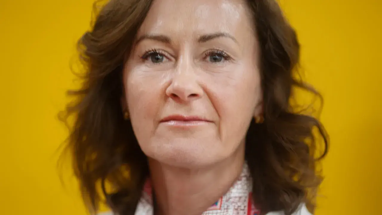 Helena Hedblom, en kvinna med brunt hår och en varm blick, poserar framför en solgul bakgrund.