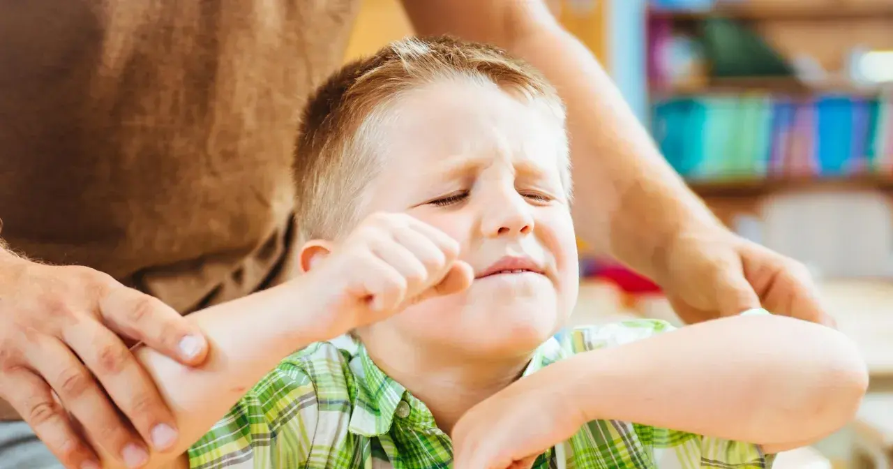 Chłopiec zamyka oczy, zaciska pięść, a dorosły trzyma go za ramię. Szukamy odpowiedzi, jak leczyć ADHD, by pomóc dzieciom.