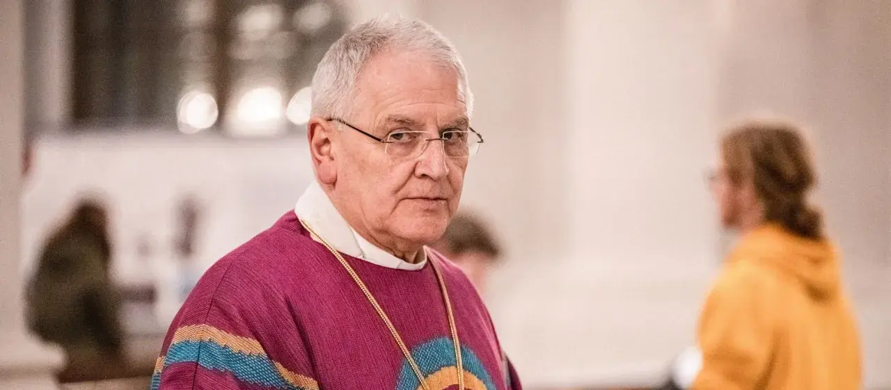 Bischof Heinrich Timmervers trägt ein violettes Messgewand mit bunten Streifen. Er blickt ernst in die Kamera.