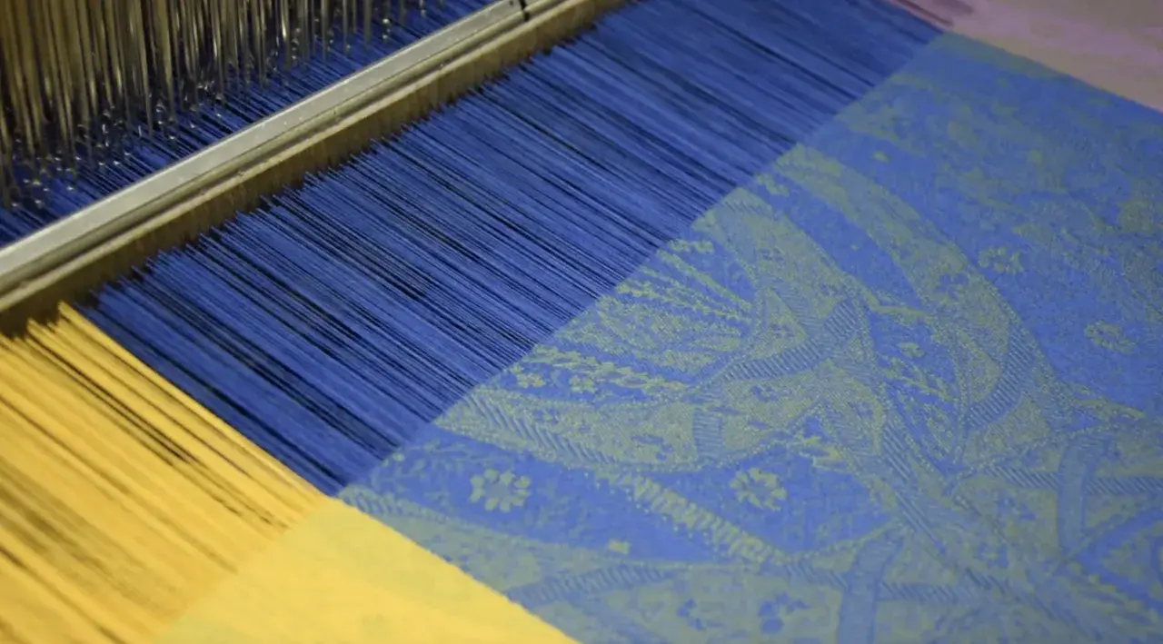 Le métier à tisser jacquard crée un motif complexe sur un tissu bleu et jaune.