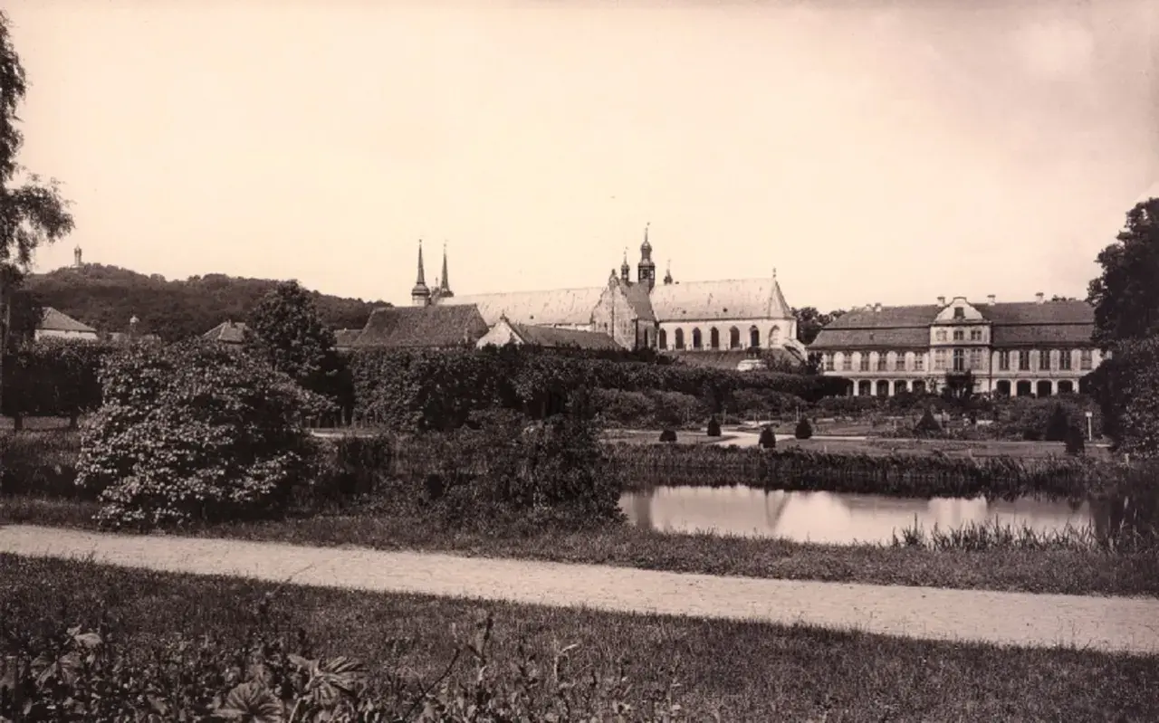 Widok na pałac opatów w Gdańsku z ogrodem i stawem. W oddali wzgórze z pomnikiem.