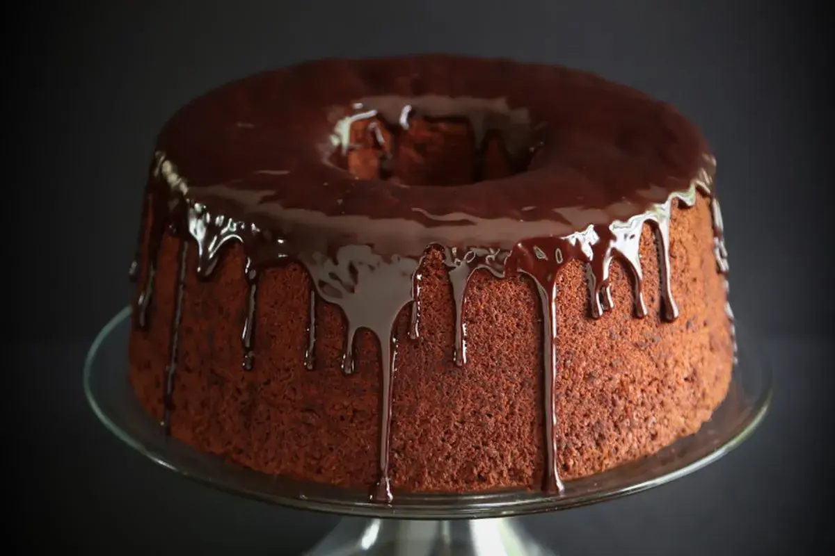 Chiffon cake al cioccolato con glassa lucida che cola. Un dolce invitante su un piatto di vetro.