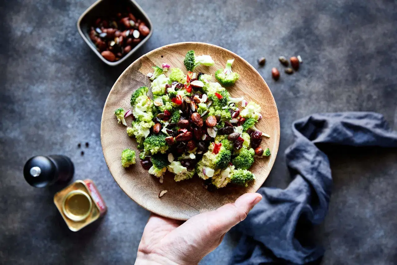 Frischer Brokkoli Salat mit Nüssen und roten Zwiebeln auf einem Holzteller, bereit zum Genießen.