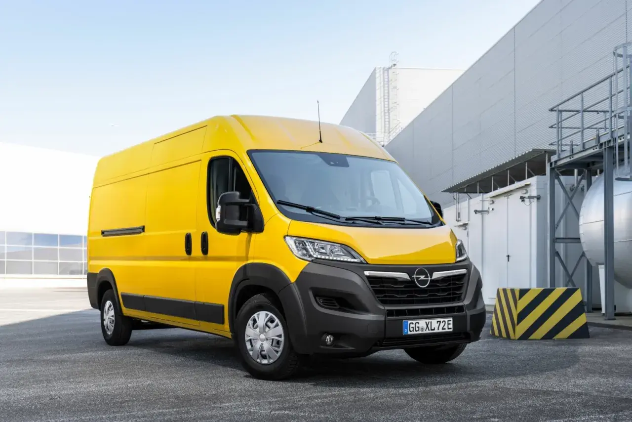 Żółty Opel Movano stoi na parkingu przed nowoczesnym budynkiem przemysłowym.