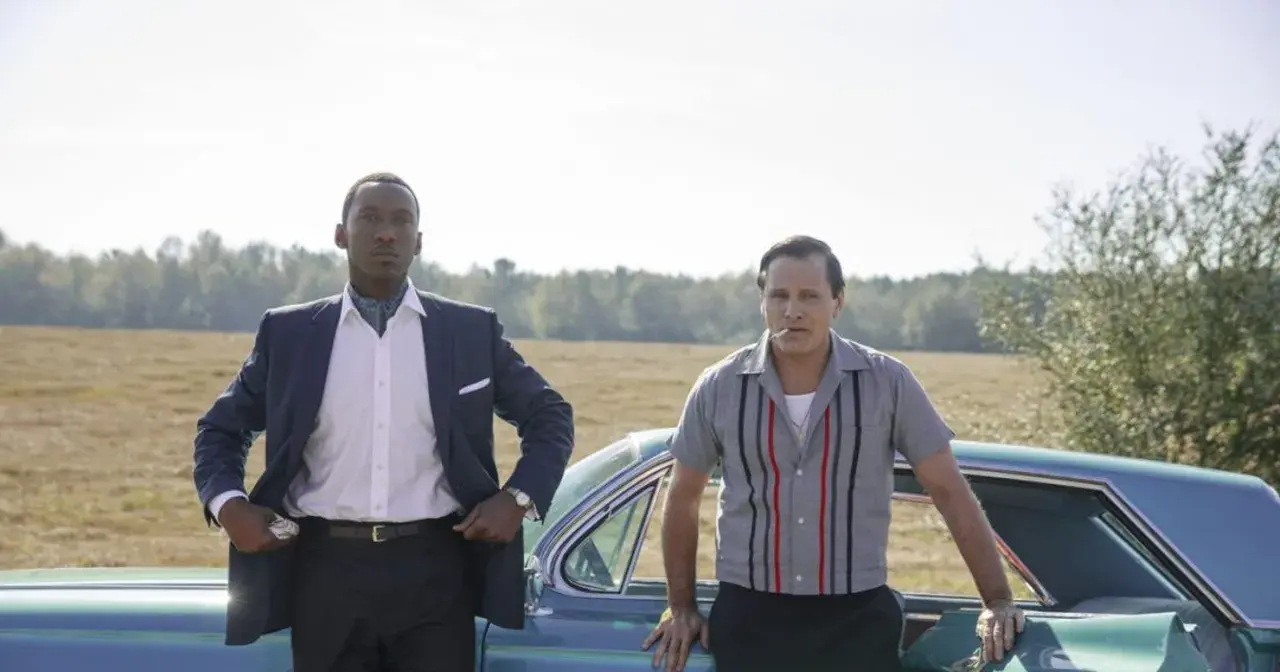 Obsada filmu Green Book: Mahershala Ali w eleganckim garniturze i Viggo Mortensen w koszuli z lat 60. stoją obok siebie przy samochodzie.