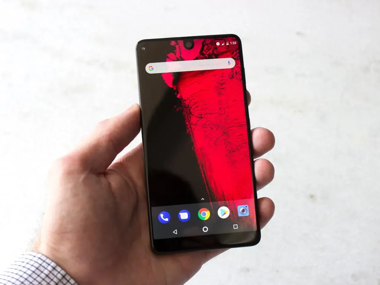 Dłoń trzyma smartfon z wycięciem (notch) na górze ekranu, wyświetlający czerwony wzór i ikonki Androida.