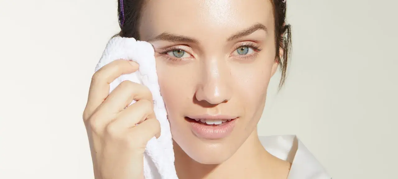 Mujer con toalla blanca limpiando su rostro, evitando el maquillaje cuarteado.