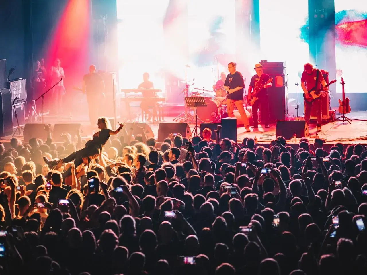 Energiczny koncert w klubie Stodoła Warszawa. Tłum szaleje, a na scenie gra zespół. Jedna z fanek jest niesiona przez publiczność.