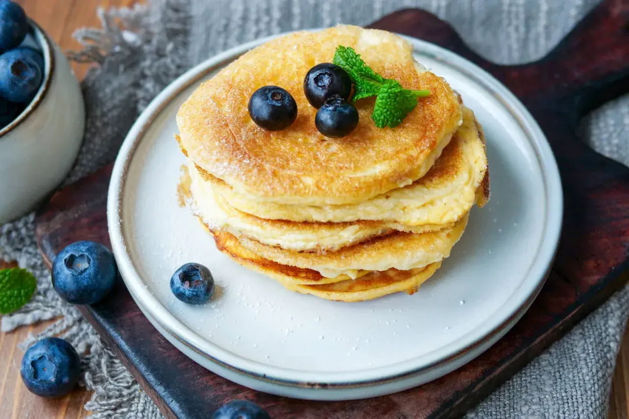 Ein Stapel fluffiger **Protein Pfannkuchen** mit Blaubeeren und Minze, bestäubt mit Puderzucker.