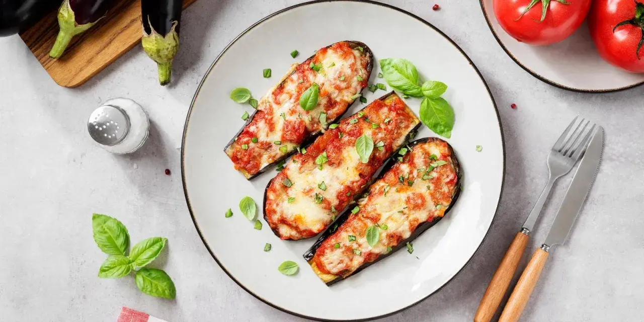 Berenjenas asadas con tomate y queso, un plato delicioso de recetas con berenjenas. Decoradas con albahaca fresca.