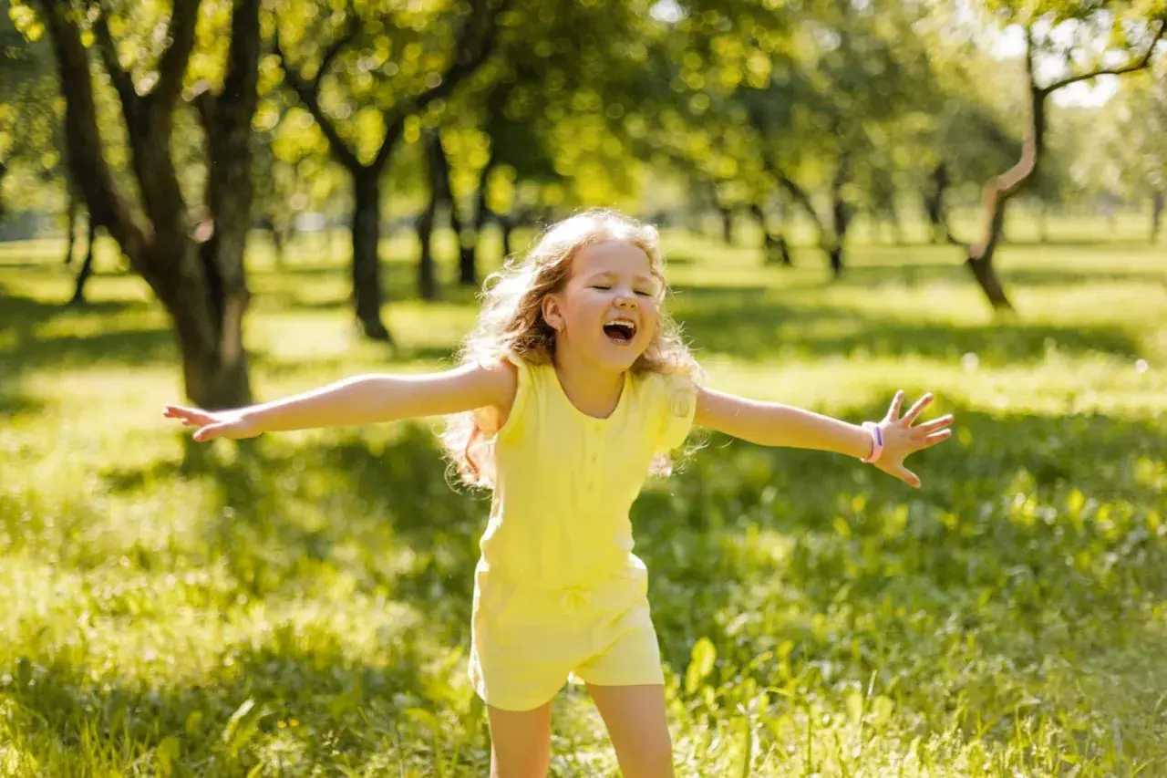 Niña feliz en un parque, disfrutando del sol. Su alegría refleja la autoestima en niños de 9 a 12 años.