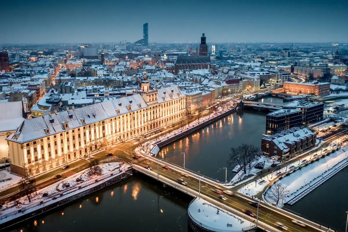 Zimowy Wrocław nocą. Ośnieżone dachy, rzeka i mosty tworzą magiczny widok. Warto odkrywać wrocławskie atrakcje zimą.